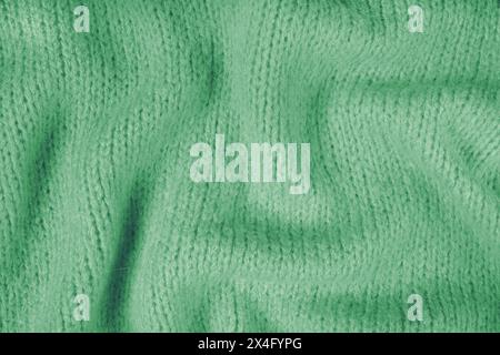 Close up background of green knitted fabric made of viscose yarn. Crumpled knitting wool, soft knitwear texture background. Abstract knitted wrinkled Stock Photo
