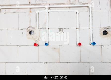 New unfinished plumbing installation exposed white PVC pipes mounted in the wall. Red and blue tubes are for hot and cold water. Stock Photo