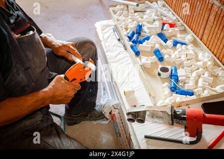 Plumber's hands as preparing polypropylene pipes to connecting them in pipeline, workshop at indoor construction site, residential building. Stock Photo