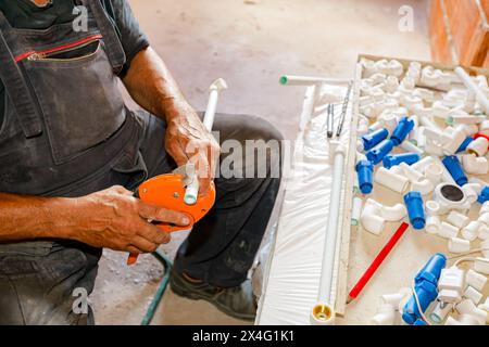 Plumber's hands as preparing polypropylene pipes to connecting them in pipeline, workshop at indoor construction site, residential building. Stock Photo