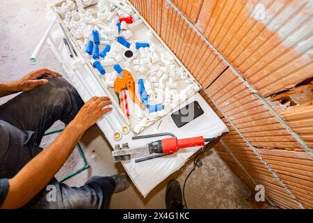 Plumber's hands as preparing polypropylene pipes to connecting them in pipeline, workshop at indoor construction site, residential building. Stock Photo