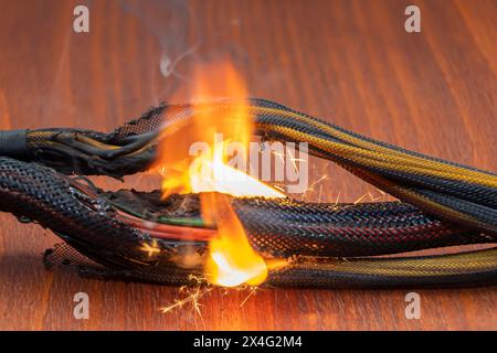 Electrical wiring and wires are lit on a dark background. A short circuit in the twisted wires from the computer. Flames, sparks and smoke. Stock Photo