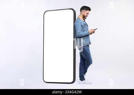 Man with mobile phone standing near huge device with empty screen on grey background. Mockup for design Stock Photo