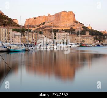 Bonifacio, Corse-du-Sud, Corsica, France. View across harbour to the citadel, dawn, the Bastion de l'Etendard reflected in tranquil water. Stock Photo