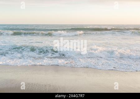 Dynamic waves break on a sunlit, sandy beach Stock Photo