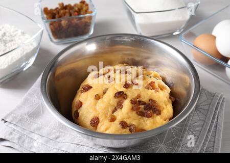 Dough with raisins in bowl and ingredients on white table, closeup Stock Photo