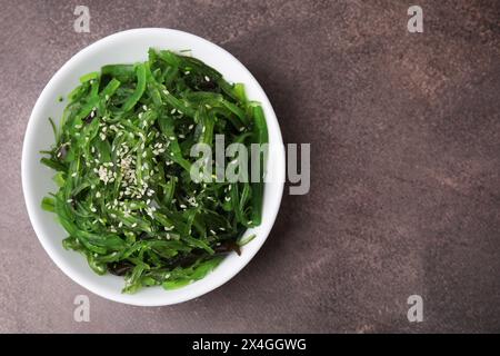 Tasty seaweed salad in bowl on brown table, top view. Space for text Stock Photo