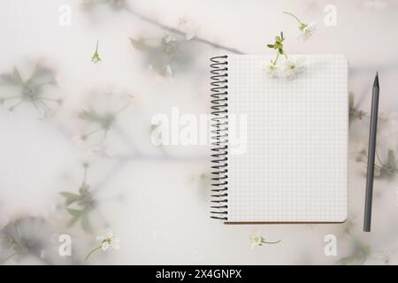 Guest list. Notebook, pencil and beautiful cherry tree blossoms on spring floral background, flat lay. Space for text Stock Photo