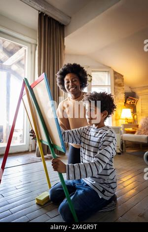 African american single mother with son drawing on board with chalks together. Family love concept. Stock Photo