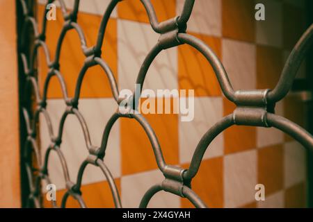 Cage metal net arranged in a pattern on yellow white tile wall background. Fence mesh. Metallic lattice in a form of rhombuses. Security concept. Stock Photo