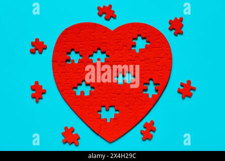 Read heart-shaped puzzle on a serene blue background, surrounded by scattered missing pieces. Love and fragmented emotions related concept. Stock Photo
