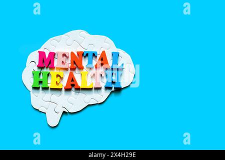 Wording "Mental Health" made of colorful wooden letters placed on top of a complete human bran puzzle on blue. Building mental well-being. Stock Photo