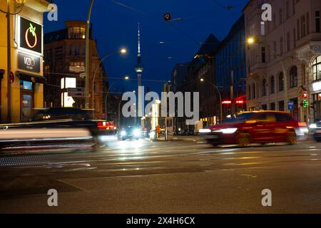 Cars driving down night Oranienburger street, Illuminated buildings and Fernsehturm TV tower visible in background, Nightlife, sustainability and envi Stock Photo