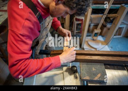Focused man carpenter measures handmade wooden bed legs with caliper. Woodworking small business. Stock Photo