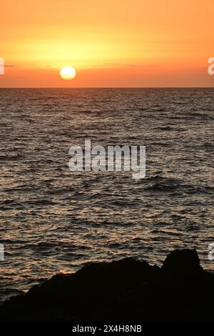 golden sunset casting a warm glow over the sea, highlighting the gentle waves and creating a peaceful and mesmerizing view of the setting sun Stock Photo