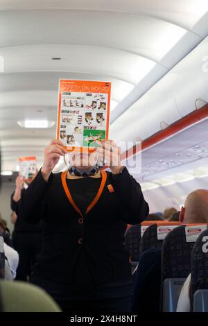 Cabin crew & safety card. Flight attendant giving pre-flight safety talk presentation to explain correct use of lifejacket, oxygen mask & seat belt. (138) Stock Photo