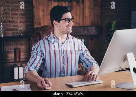 Photo of nice young corporate man use computer think wear striped shirt loft interior office indoors Stock Photo