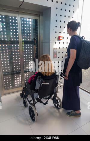 Child teenager daughter / girl kid aged 14 years sitting in wheelchair, using lift elevator for disabled people, with mum. Split airport. Croatia. (138) Stock Photo