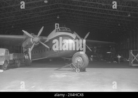 England c.1957 – A photograph of the Dan Air Bristol Type 170 Freighter Mk.31E, registration G-AINL parked within a maintenance hangar. This aircraft, serial number, 012827, was manufactured by The Bristol Aeroplane Company Ltd in 1947. It was obtained by Dan Air in July 1957 from Aviation Traders Ltd, having previously served with the Royal Air Force and Aer Lingus. It was the first of three of its type to go into service with Dan Air. A Bedford O Type flatbed truck is parked under the wing and a replacement aircraft wheel is on a trolley in the foreground. Stock Photo