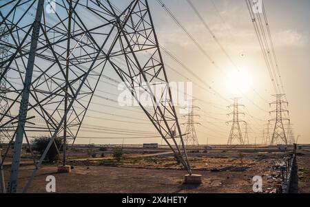 Large tall steel power pylons in rather flat landscape of Saudi Arabia, only black silhouettes visible against bright afternoon sun Stock Photo