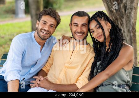 Three young, multicultural friends - smiling and embracing in an urban park, showcasing joy and friendship - relaxed, happy. Stock Photo