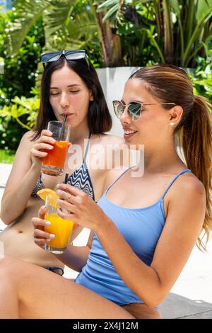 Two friends drinking smoothies by a swimming pool Stock Photo