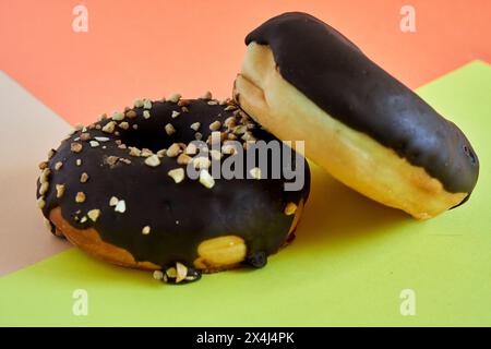 two Chocolate covered donuts with crush nuts on top on colored background Stock Photo