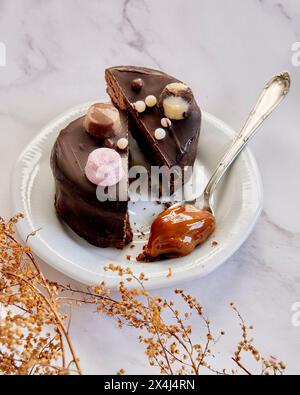 Artisan chocolate alfajor argentinian broken in half on a white plate with a spoon of dulce de leche Stock Photo