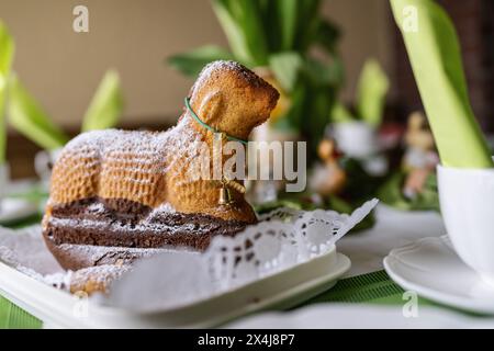 Close-up of a lamb-shaped Easter cake with sugar dusting on a decorated table. Stock Photo