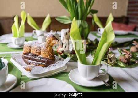 Easter-themed table setting with cake lamb dusted with powdered sugar, tulips, and decorations Stock Photo