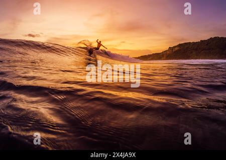 December 14, 2022. Bali, Indonesia. Man during surfing with sunset or sunrise tones. Pro surfer riding on wave and make tricks. Stock Photo