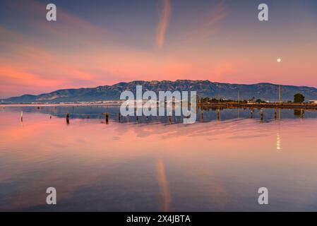 Sunrise in the Alfacs bay in the Ebro Delta, with the Montsià mountain range in the background and the full moon (Tarragona, Catalonia, Spain) Stock Photo