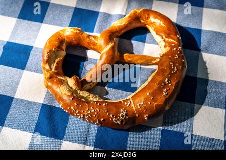 Bavarian deliciousTraditional freshly baked pretzel on blue and white checkered tablecloth with sunlight and shadows. German Oktoberfest concept image Stock Photo
