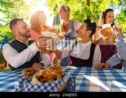 Friends sitting in beer garden or oktoberfest with beer glasses toasting to each other in Bavaria, Germany Stock Photo