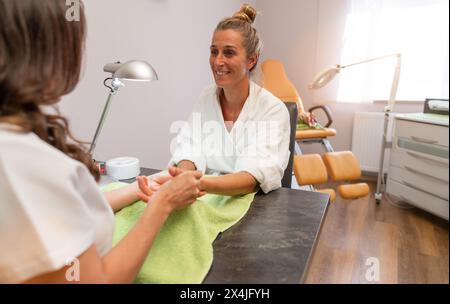 Smiling woman receiving a massage in a beauty salon with a manicurist working on her nails Stock Photo