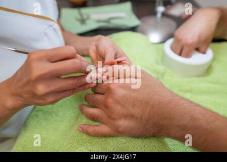 Manicurist performing a manicure, focusing on a client's nails with a cuticle pusher being used over a green towel Stock Photo