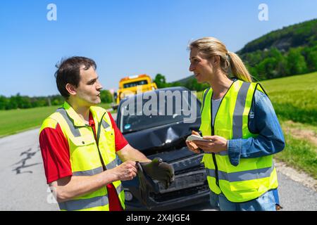 Roadside assistance worker and customer discuss what to do next after an accident beside a towed car and tow truck in the background Stock Photo