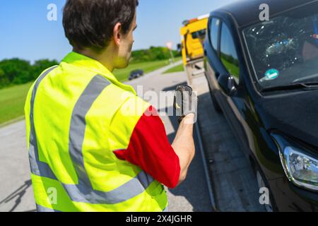 Tow truck operator uses a remote control to load an accident car onto the tow truck Stock Photo