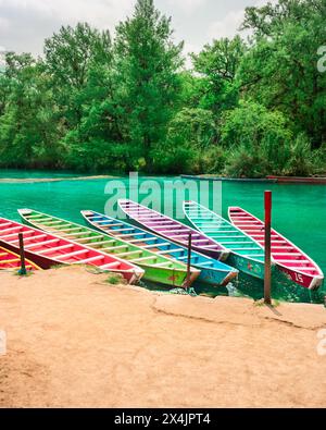 Six colorful wooden boats parked on the bank of a beautiful Huasteca river in El Esalto del Meco Mexico, with the tropical forest in the background Stock Photo