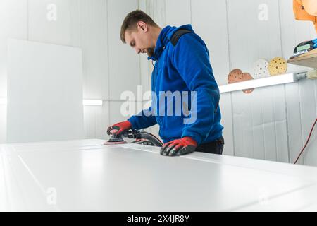 Professional male carpenter using electronic sander tool in wood workshop, male joinery work on wood production and renovation of wooden furniture. High quality photo Stock Photo