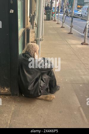 Depressed looking homeless man sits along  an empty sidewalk in the early morning  in midtown Manhattan. Stock Photo