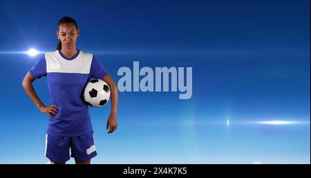 Image of african american female football player holding ball, over blue background with lights Stock Photo