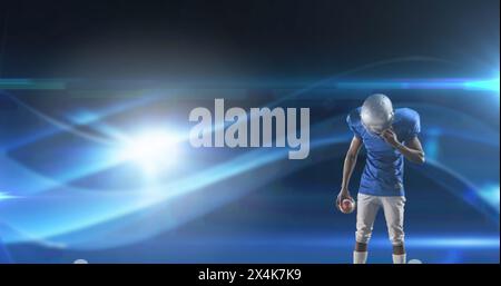 Image of excited american football player holding ball on dark background with moving lights Stock Photo
