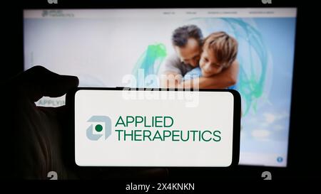 Person holding cellphone with logo of American biopharmaceutical company Applied Therapeutics Inc. in front of webpage. Focus on phone display. Stock Photo
