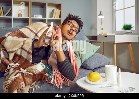 Sick indian man lying on sofa under a blanket at home, feeling unhealthy with influenza. Stock Photo