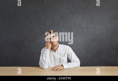 Portrait of young pensive male employee sitting at table and bored, tired and need relax day. Stock Photo