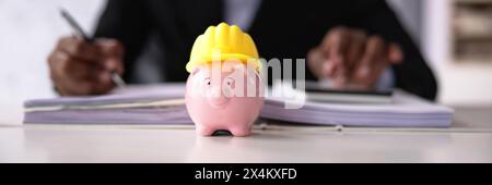 Hard hat wearing construction worker holding piggy bank Stock Photo