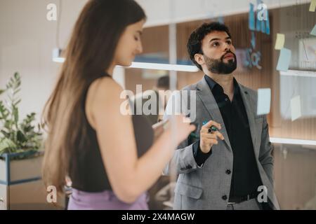 Business colleagues brainstorming with sticky notes on a glass wall in modern office setting Stock Photo