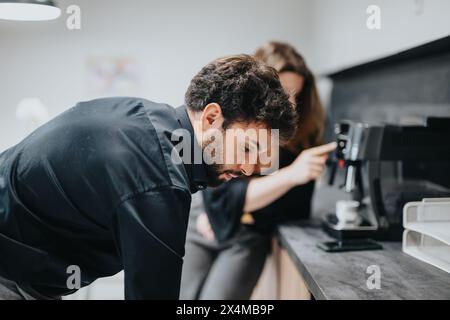 Office coffee break: Couple of coworkers engaged in a casual conversation by the espresso machine Stock Photo