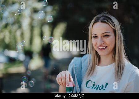 Smiling young woman enjoying a sunny day at the park with soap bubbles around Stock Photo